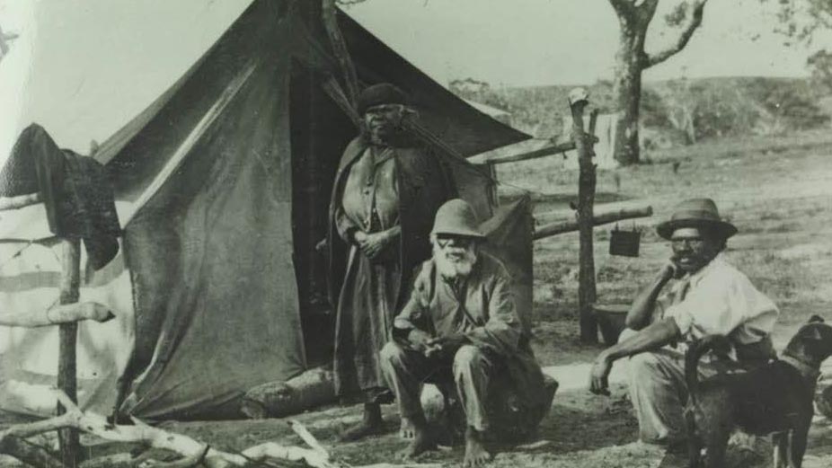 两名土著男子和一名土著女子站在帐篷前