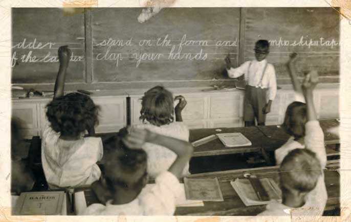 教室里的土著儿童。一些学生举手了，一个学生站在教室前面的黑板前，上面写着草书。