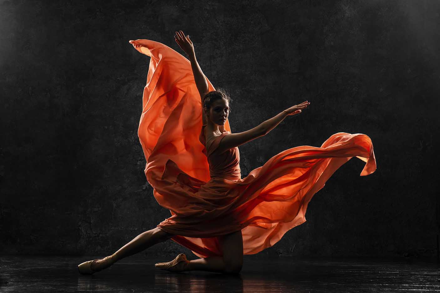 一个年轻的芭蕾舞演员的剪影照片穿着长桃红色连衣裙，足尖鞋与丝带。
