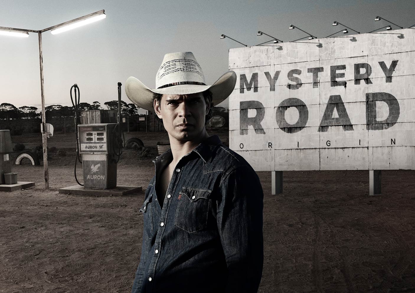 一名戴着牛仔帽的男子站在加油站浏览器前，广告牌上写着“神秘之路”。