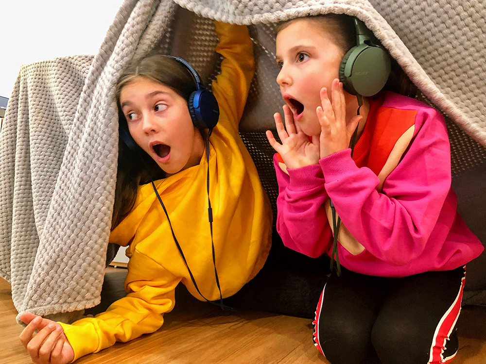 两个戴着耳机的女孩从毯子堡垒里往外看