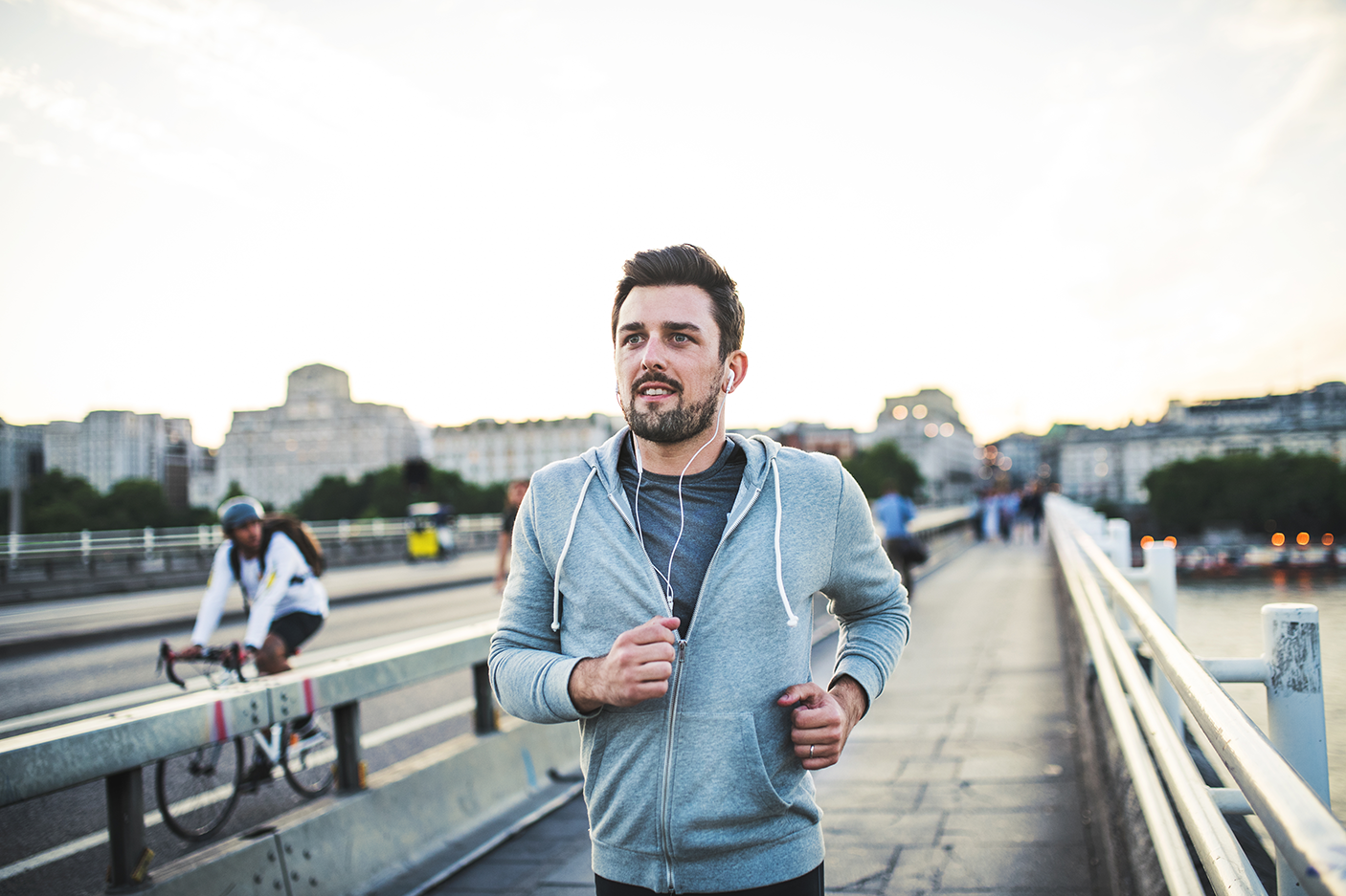 年轻的运动男子戴着耳机在城外的桥上跑步。- - -库存图片