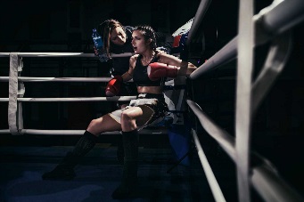 一位女拳击手坐在拳击台角落的照片。她正在听取教练的建议。